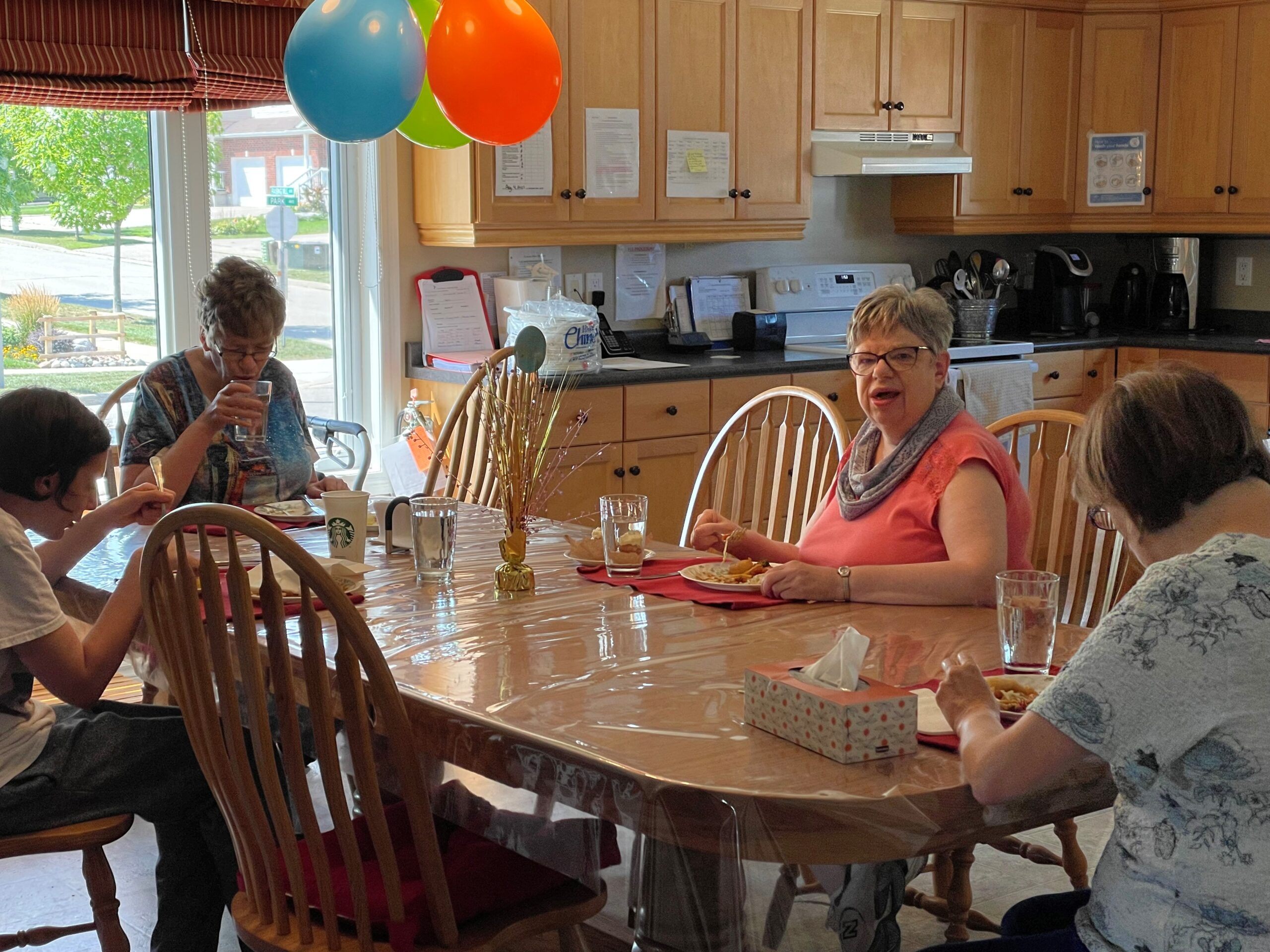 4 individuals sitting at a wooden table in a kitchen with balloons in the background
